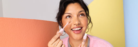 A woman holding a silky blur hydrating concealer, applying the product to her face. 