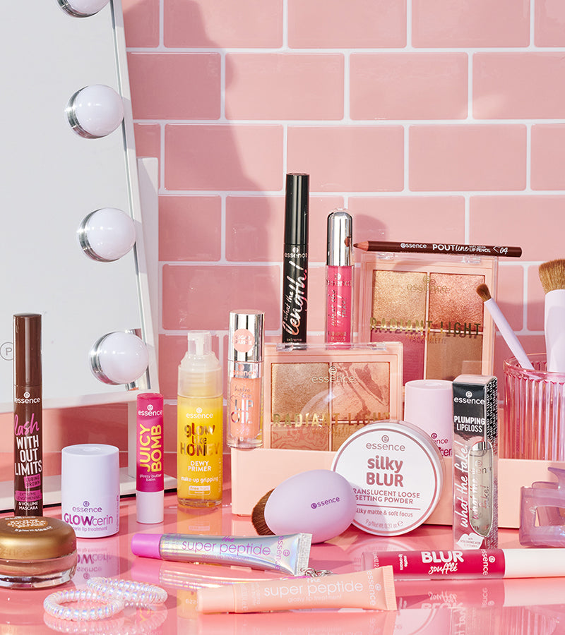 Collection of Essence makeup products on a pink surface with a mirror in the background.