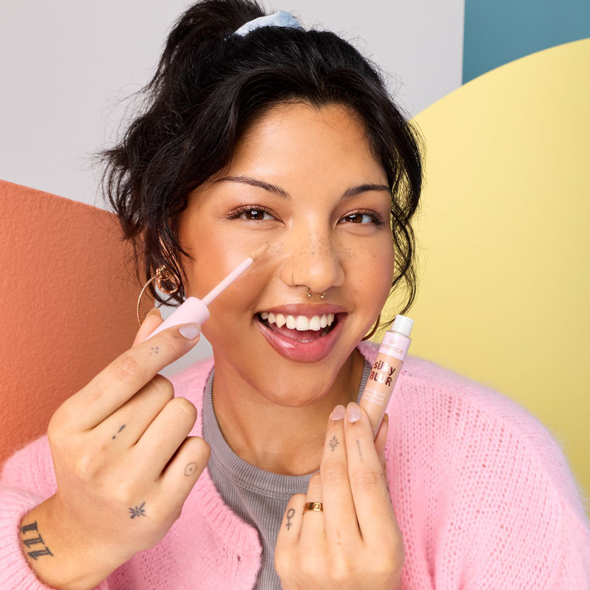 Woman holding a concealer against a colorful background