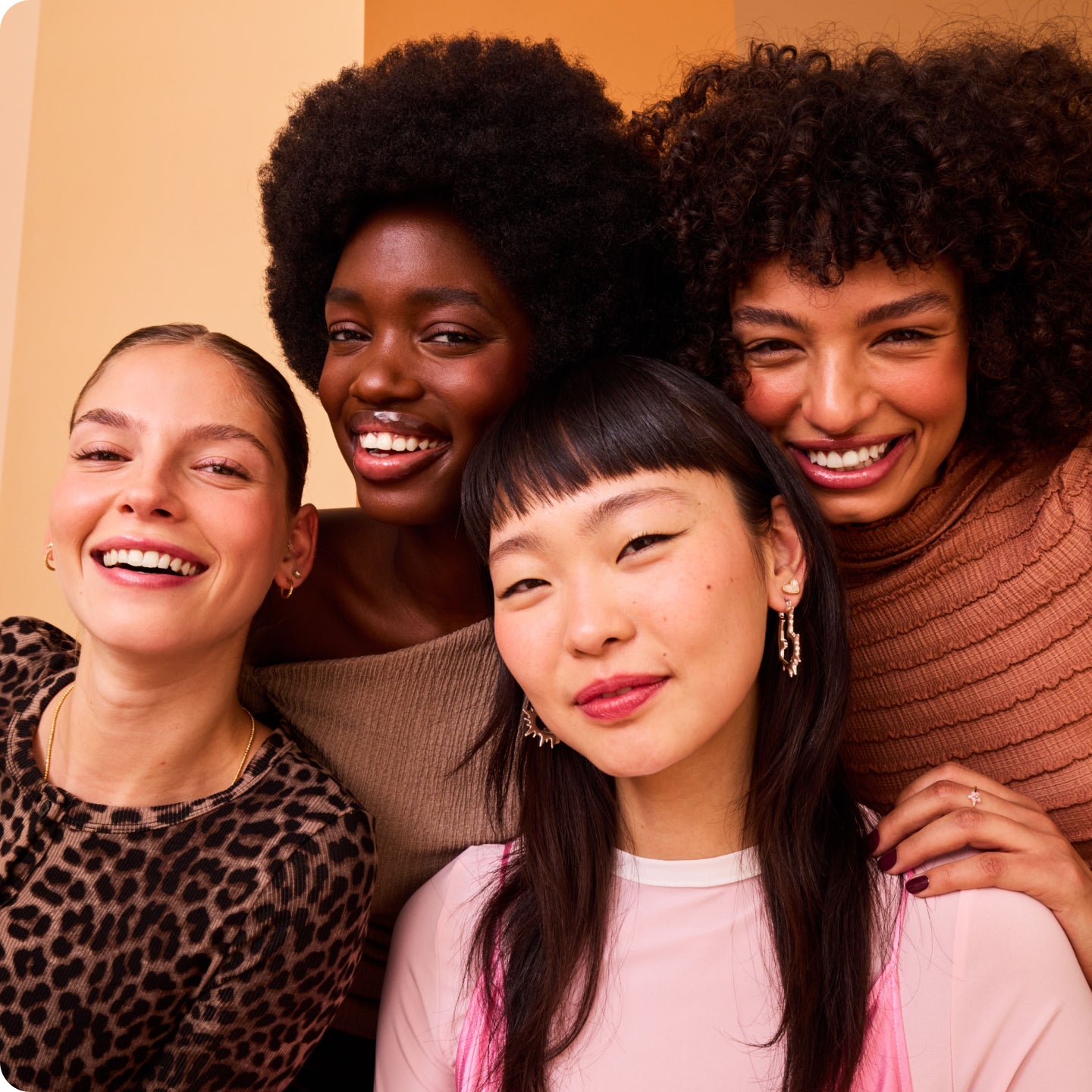 Four women posing together against a warm-toned background